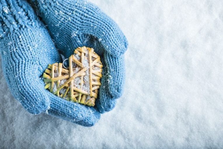 Female hands in teal knitted mittens with a entwined heart