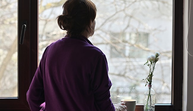 woman looking out window during quarantine