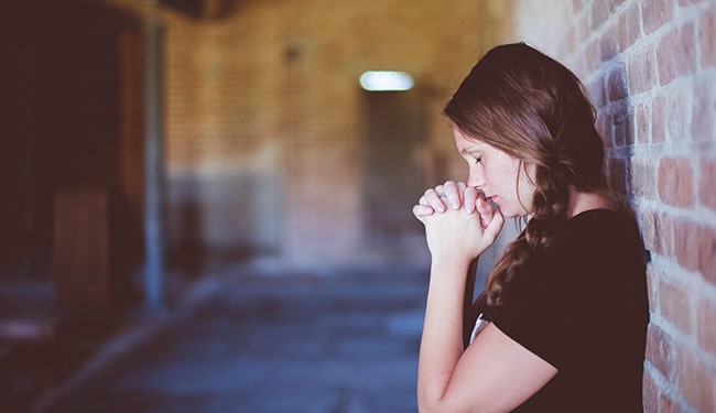 woman praying leaning back on wall