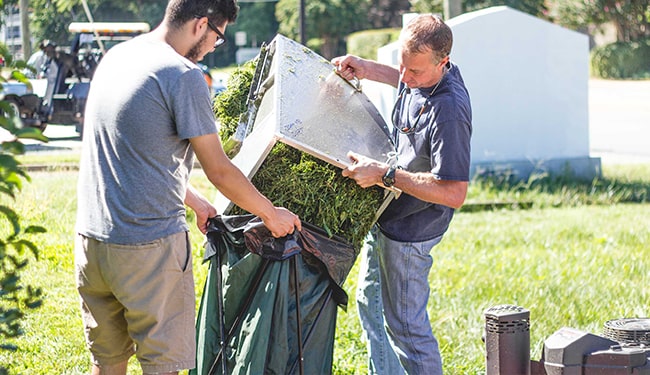 men pouring cut grass into bag