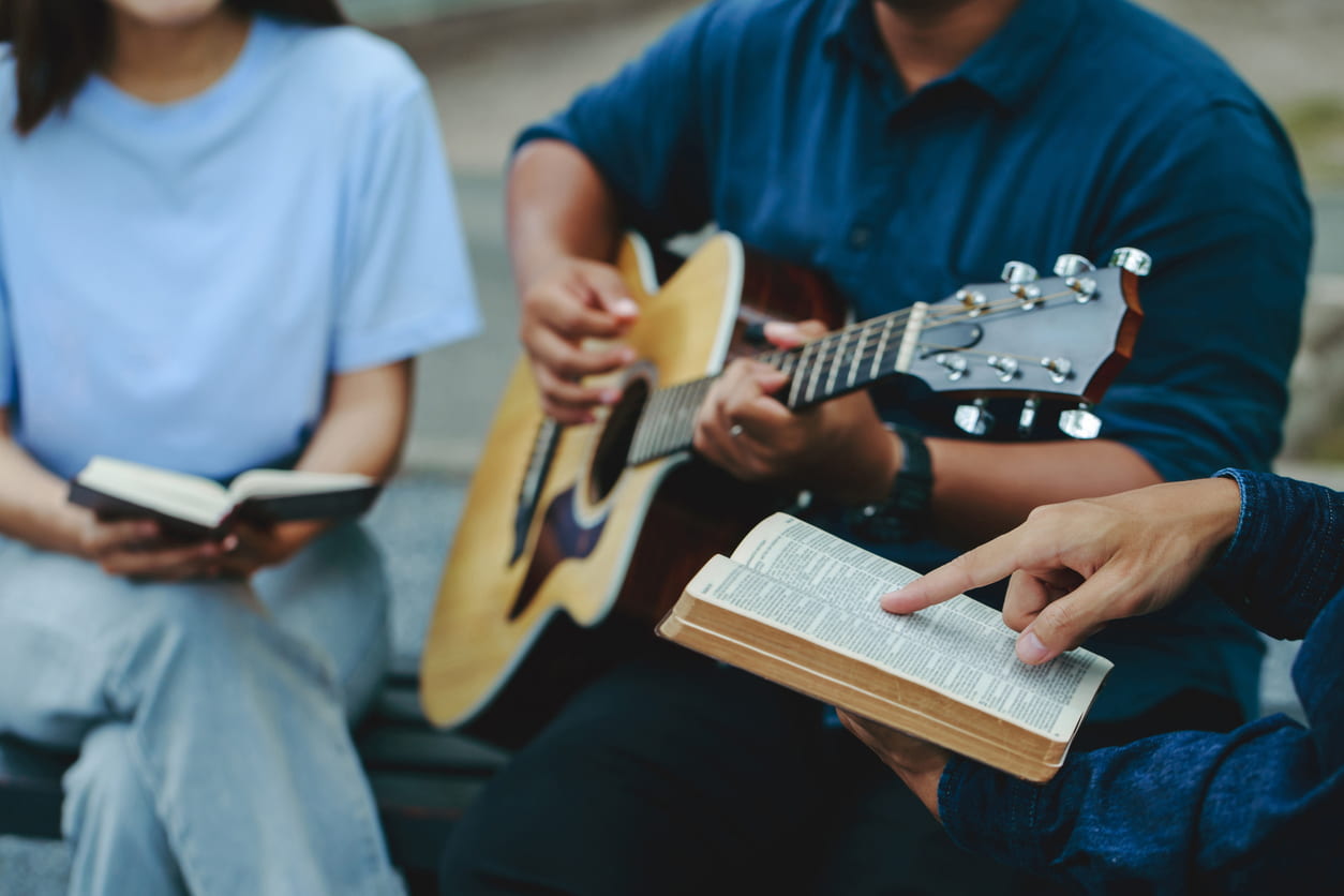 Christian families worship God in the garden by playing guitar and holding a holy bible. Group Christianity people reading the bible together