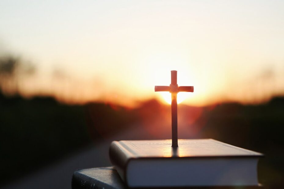 cross on top of bible during sunset