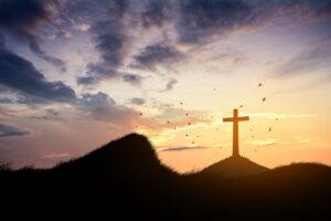 religious cross on hill during sunset with birds flying in background