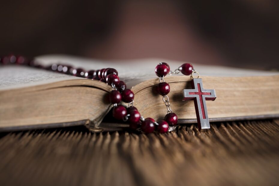 red rosary laying on top of open bible