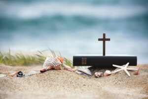bible and cross on sandy beach with sea shells